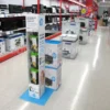 Cardboard retail display unit showcasing HP printer inks, equipped with eurohooks and vibrant printed branding, placed in an electronics store aisle.