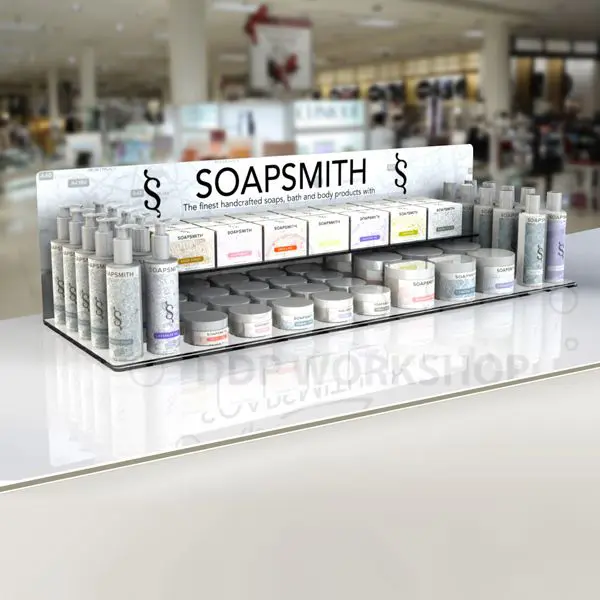 Double-tiered acrylic retail display stand holding Soapsmith bath and body products on a countertop in a department store.