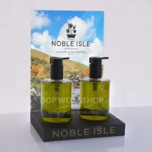 Point of sale display stand with two green pump bottles and an A4 graphic insert reading “Noble Isle”.