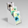 A compact white 3-tier acrylic display stand showcasing A5 portrait greeting cards with floral designs.