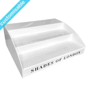 Three-tier white acrylic cosmetic display stand with “Shades of London” branding on the front lip.