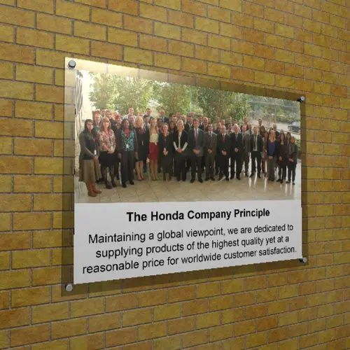 Wall-mounted printed acrylic frame displaying a group staff photo with a caption titled "The Honda Company Principle" and a corporate mission statement.