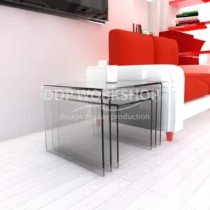 Set of three clear acrylic nesting tables arranged beside a white and red modern sofa on a white wood floor.