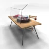 Transparent tabletop food screen sneeze guard covering a cake on a wooden table with a chair and glass of wine beside it