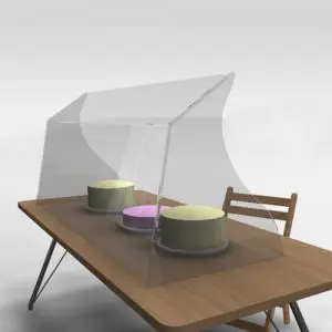 Side-profiled clear acrylic food guard displayed on a wooden table, covering three round cakes with a chair in the background.