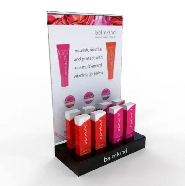 Balmkind lip balm retail counter display with vibrant packaging, branded black acrylic base, and large promotional back panel.