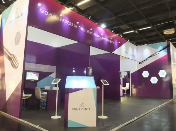 Bespoke trade show exhibition stand for Prima Dental featuring branded graphics, product displays, and interactive iPad stations in a modern booth design.